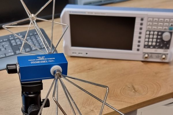 Bikonische Messantenne auf Stativ, dahinter der Spektrumanalysator auf der Werkbank